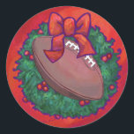Adesivo Futebol de Wreath de Natal em Red<br><div class="desc">O futebol em um Natal sobre ornamentos Vermelhos Textuturados, presentes e decorações divertidas apresenta nossa arte original de futebol, toda decolada para as festas de dentro, uma coroa verde holly com um arco vermelho e um fundo vermelho com nossa textura de assinatura. Esta bola divertida de esporte decorada em feriado...</div>