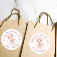 Urso de peluche rosa com balões sobre nuvens, sob 