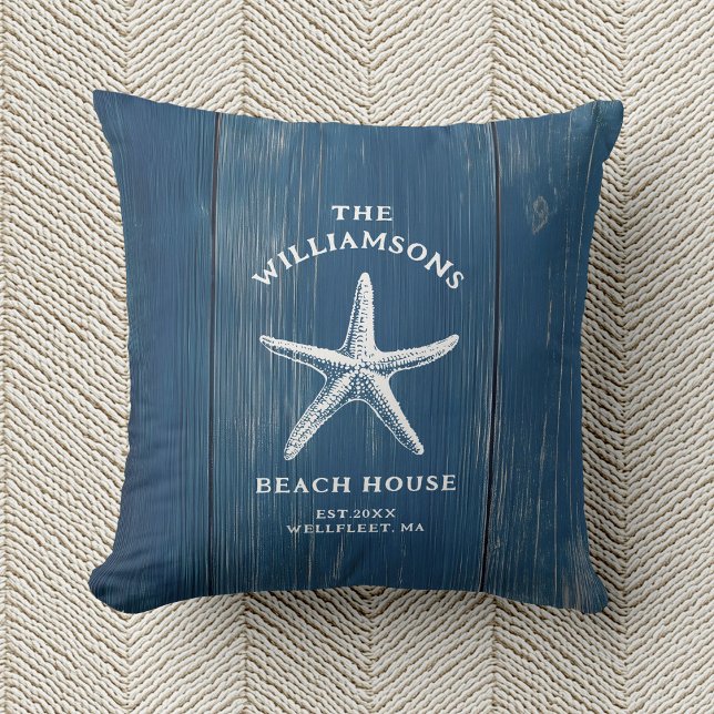 Almofada Casa Azul Costeira de Starfish (A blue pillow with a white starfish and text reading "The Williamsons Beach House" rests on beige)