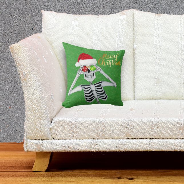 Almofada Esqueleto Sorridente Segurando Ornamentos para Olh (Happy Merry Christmas Skeleton in Santa hat with ornaments on green throw pillow.)
