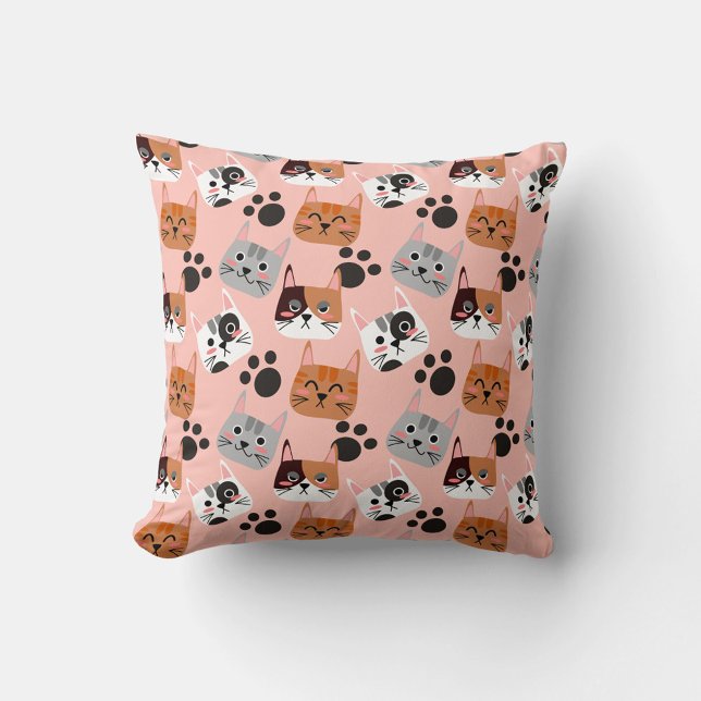 Almofada Rostos de Gato (A flat lay shot shows a square pillow with a pink background and a repeating pattern of cartoon cat.)