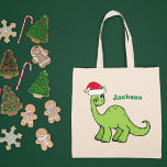 Bolsa Tote Bonito Dinossauro de Natal Personalizado Nome para<br><div class="desc">Dinossauro verde fantástico que parece muito bonito num chapéu vermelho de Papai Noel,  de férias,  com um sorriso. Adoráveis garotos personalizados para o presente do seu filho ou menina.</div>