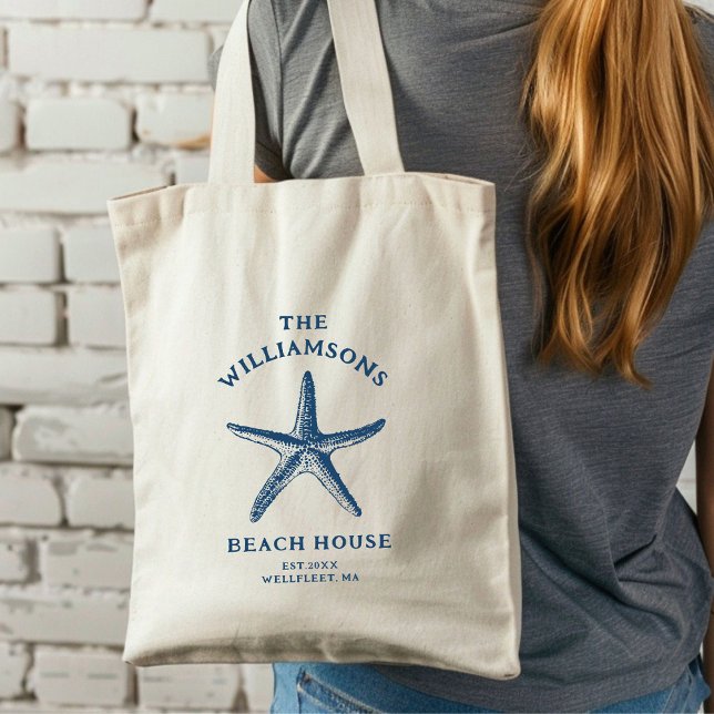 Bolsa Tote Casa Azul Costeira de Starfish (A woman with long hair carries a cream tote bag featuring a blue starfish design.)