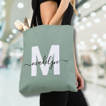 Bolsa Tote Monograma do Nome do Script Moderno Verde Sage<br><div class="desc">Sage Green Trendy Modern Script Name Monograma Tote Bag Personalizado Adicione um toque de sofisticação ao seu estilo do dia a dia com este saco de tote chic. Apresentando uma inicial branca elegante centrada num fundo verde de sábio suave, sobreposta com um nome de script preto fluente, esta design limpa...</div>