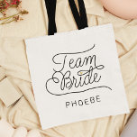 Bolsa Tote Nome de Casamento Dourado do Script Moderno da Equ<br><div class="desc">Esta bolsa de tote moderna com um script de chic casual minimalista que lê design TEAM BRIDE, assim como o nome personalizado da sua madrinha de casamento ou dama de honra, apresenta linhas limpas para criar uma aparência elegante e sofisticada. O estilo subestimado com os pequenos detalhes cardíacos de ouro...</div>