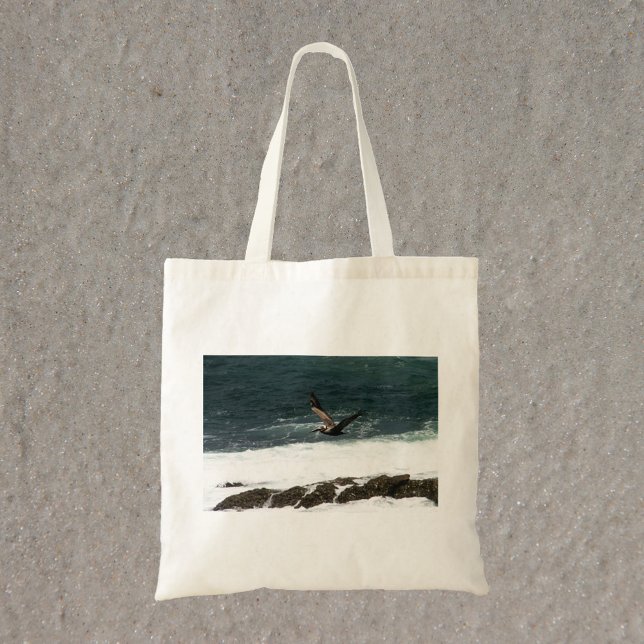 Bolsa Tote Pelican voando sobre fotografia do oceano Pacífico (A tote bag with a photograph of a pelican flying over the Pacific Ocean)