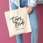 Bolsa Tote Pincel Chic Tendência Preto Equipe da Noiva Script<br><div class="desc">Bolsa tote de casamento com as palavras "Team Bride" em um estilo de letra cursiva preta e elegante,  perfeita para damas de honra,  madrinha e menina de flores. Para outros itens correspondentes,  veja aqui https://www.zazzle.com/collections/119250194970828530?rf=238364477188679314</div>