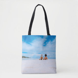 Bolsa Tote Two women lying on white sand facing beach under b
