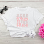 Camiseta Aqui Vem A Festa de solteira Da Noiva<br><div class="desc">Camiseta de festa de solteira da noiva bonita com "Here Comes The Bride" em uma fonte grande,  rosa e esticada,  estilo 70,  e ilustração de uma margarida. A camiseta "Aqui Vem A Parte" está disponível para o esquadrão de solteiros.</div>