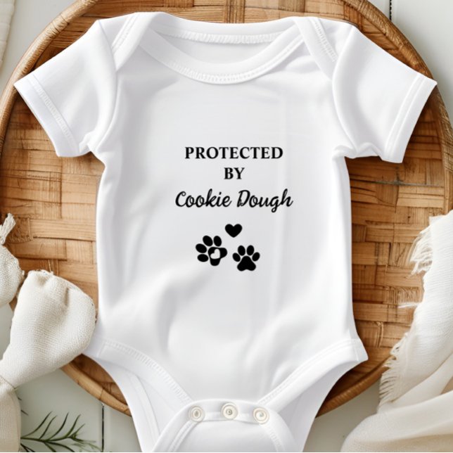 Camiseta Cuja proteção é personalizada por cão (Adorable baby bodysuit with "Protected by (Dog's Name)" design, featuring hearts and paw prints.)