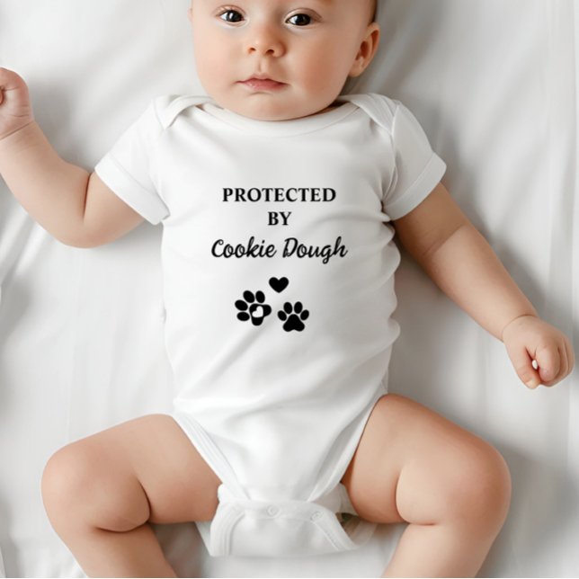 Camiseta Cuja proteção é personalizada por cão (Adorable baby bodysuit with "Protected by (Dog's Name)" design, featuring hearts and paw prints.)