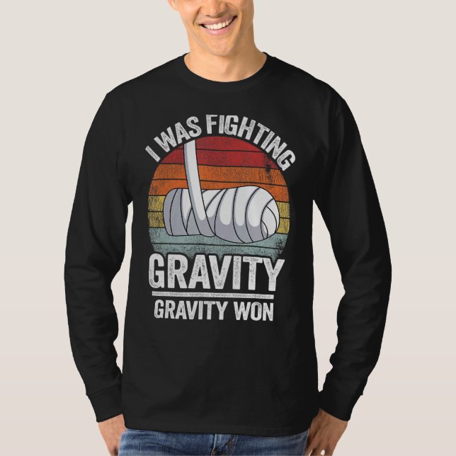 Camiseta Eu Estava Lutando Com Gravidade Ganhei Mão Quebrad (Frente)
