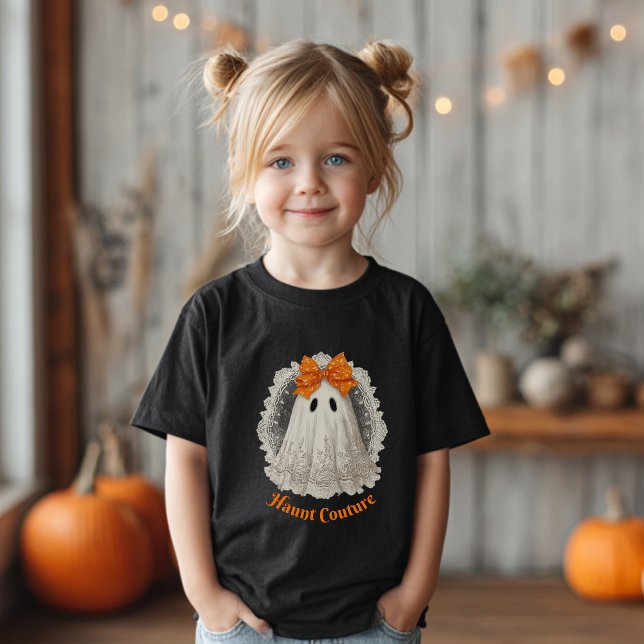 Camiseta Moda Assombrada em Renda Fantasma com Laço Laranja (Girl with blond pigtails wearing a black T-shirt with a ghost &"Haunt Couture".)