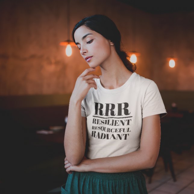 Camiseta RRR - Resiliente, Recursos, Radiante (Young woman in thoughtful pose wearing a "RRR: Relilient, Resourceful, Radiant" white t-shirt.)