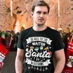 Camiseta Seja gentil com os Papais noeis do garçom.<br><div class="desc">Lembre seus clientes de ficarem na lista legal este ano com esta divertida e adorável camiseta de Natal com a redação "Seja gentil com o garçom, os Papais noeis estão assistindo" em fontes pretas modernas, decoradas com luzes de Natal vermelhas, verdes e amarelas, flocos de neve pretos, um chapéu vermelho...</div>