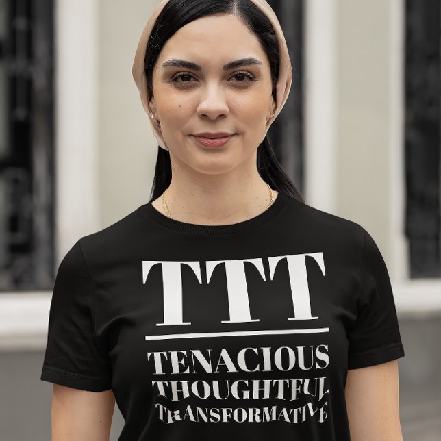 Camiseta TTT - Tenaz, Cuidadosa, Transformativa (Young woman wears a "TTT: Tenacious, Thoughtful, Transformative" black t-shirt.)