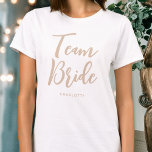 Camiseta White Beige Personalizado de Casamento de Noiva da<br><div class="desc">Celebre o seu esquadrão noivo com esta t-shirt personalizada do casamento! As palavras 'Team Bride' são escritas em uma fonte de script de tendência e abaixo você pode adicionar um nome personalizado, data de casamento, local ou outro texto. Um presente adorável para um fim de semana de festa de solteira,...</div>