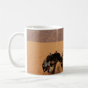 CANECA DE CAFÉ DOIS CAMELOS SENTADOS NA AREIA MARROM PERTO DAS MO