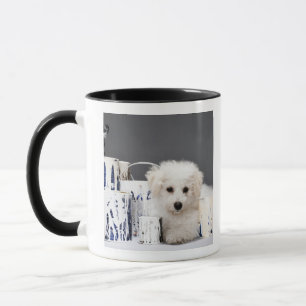 Caneca Filhote de cachorro que senta-se entre latas da