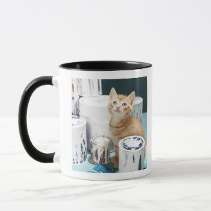 Caneca Gatinho que senta-se entre latas da pintura