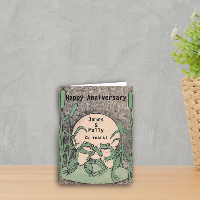 Cartão 25a lua feliz da almofada de lírio dos sapos (Two cute argueing green frogs on lily pad full moon on Happy anniversary card.)