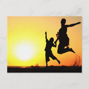 Cartão Postal Silhuetas da mãe e do filho saltando na praia ao s