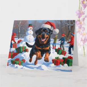 Cartão Rottweiler Correndo na Neve com Chapéu de Natal