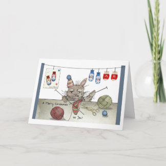 Cartão Um coelho tricotando um chapéu de Natal