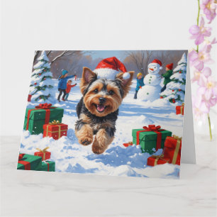 Cartão Yorkipoo Correndo na Neve com Chapéu de Natal