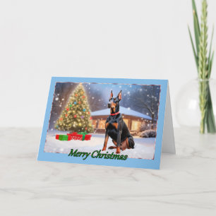 Doberman com cartão de Natal em árvore