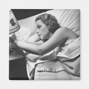 Íman Jovem deitada na cama desligando a lâmpada