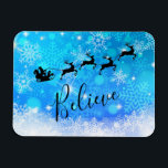 Íman Papai Noel e sua Rebelde Voadora - Acredite<br><div class="desc">Íman de Natal - estilo flexível,  com uma silhueta preta de papais noeis cavalgando em seu trenó sendo puxado por sua rena voando pelo céu. Acredite que está escrito em uma fonte de script de tendência. O fundo é um design de floco de neve gelado azul gelado.</div>