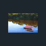 Impressão Em Tela Red Boat Reflection on Serene River<br><div class="desc">This evocative image captures a vibrant red wooden boat resting peacefully on the glassy surface of a river. The composition is defined by a striking contrast between the deep, earthy tones of the water’s reflection and the brilliant, clear blue sky mirrored in the foreground. Dense green foliage lines the distant...</div>