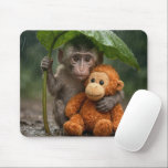 Mousepad Macaque Monkey with a Stuffed Orangutan<br><div class="desc">A young macaque monkey uses a large green leaf as a makeshift umbrella while holding onto a stuffed orange orangutan toy in the gentle rain of a lush forest</div>