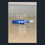 Numeração De Mesa Garrafa na praia Areia Nomes de Convidados<br><div class="desc">Esta design apresenta uma garrafa na praia. A bela cor azul da garrafa contrasta com a areia ouro, criando uma combinação perfeita. A borda branca fina enquadra perfeitamente a garrafa azul lavada na areia e combina com a tipografia branca moderna. Design de praia romântica com uma mistura de simplicidade e...</div>