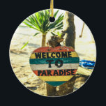 Ornamento De Cerâmica Bem-vindo ao Paraíso Beach Ocean<br><div class="desc">Bem-vindos ao paraíso Beach Ocean Linda praia de areia macia com uma palmeira verde ao fundo. Este sinal é pintado em vermelho,  amarelo,  azul e branco e lê BEM-VINDO AO PARADISE.</div>