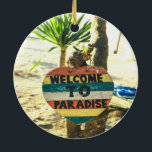 Ornamento De Cerâmica Bem-vindo ao Paraíso Beach Ocean<br><div class="desc">Bem-vindos ao paraíso Beach Ocean Linda praia de areia macia com uma palmeira verde ao fundo. Este sinal é pintado em vermelho,  amarelo,  azul e branco e lê BEM-VINDO AO PARADISE.</div>