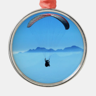 Ornamento De Metal Paraglider no fundo azul com montanhas