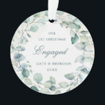 Ornamento Eucalyptus Greenery Wreath Envolvido Foto<br><div class="desc">Enfeite acrílico elegante com uma coroa composta por folhas de eucalipto e verde com uma dica de azul com "Nosso Primeiro Natal Envolvido" juntamente com seus nomes e ano em verde escuro sobre uma lavagem a aquarela pastel. A parte de trás tem sua foto de noivado favorita. Este ornamento botânico...</div>