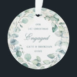 Ornamento Eucalyptus Greenery Wreath Envolvido Foto<br><div class="desc">Enfeite acrílico elegante com uma coroa composta por folhas de eucalipto e verde com uma dica de azul com "Nosso Primeiro Natal Envolvido" juntamente com seus nomes e ano em verde escuro sobre uma lavagem a aquarela pastel. A parte de trás tem sua foto de noivado favorita. Este ornamento botânico...</div>