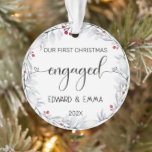 Ornamento Watercolor Wreath Nosso Primeiro Natal Envolvido<br><div class="desc">Celebre um marco especial com este adorável ornamento "Nosso Primeiro Natal Envolvido". Apresentando uma delicada coroa aquosa, enfeitada com cinzas macios e bagas vermelhas, esta ornamentação faz uma manutenção significativa para casais recém-engajados. Adicione seus nomes e ano para criar uma lembrança personalizada que captura a alegria deste Natal inesquecível. Uma...</div>