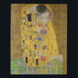 Os amantes beijando o abraço de Gustav Klimt<br><div class="desc">A luz do sol brilha do abraço do ouro que rodeia os amantes da obra-prima de Gustav Klimt, The Kiss. A cena é um paradoxo de intimidade e isolamento. O casal está sobre um precipício, um campo de flores coloridas em seus pés, mas elas estão indiferentes ao mundo ao seu...</div>