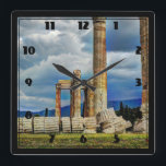 Relógio Quadrado Ruínas antigas na Grécia de Atenas<br><div class="desc">Fotografia das antigas ruínas de um templo esquecido há muito tempo em Atenas, Grécia. Podem ver-se grandes colunas verdes em pé, assim como peças danificadas e quebradas. Ao fundo pode-se ver montanhas azuis vívidas. O céu é cheio de nuvens tempestuosas que produzem um efeito temperamental. O processamento extra de fotos...</div>