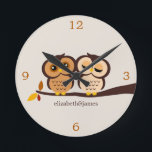 Relógio Redondo Corujas no outono<br><div class="desc">O pulso de disparo de parede feito sob encomenda do desenhista caracteriza uma ilustração adorável do vetor de um par corujas empoleiradas em um ramo em máscaras bonitas da queda do marrom, da laranja e do bege. Personalize com seu nome, monograma, iniciais, ou uma data especial tal como seu aniversário...</div>