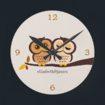 Relógio Redondo Corujas no outono<br><div class="desc">O pulso de disparo de parede feito sob encomenda do desenhista caracteriza uma ilustração adorável do vetor de um par corujas empoleiradas em um ramo em máscaras bonitas da queda do marrom, da laranja e do bege. Personalize com seu nome, monograma, iniciais, ou uma data especial tal como seu aniversário...</div>