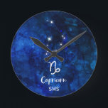 Relógio Redondo Monograma do céu da galáxia da constelação do<br><div class="desc">Design do monograma do céu da galáxia da constelação do zodíaco do Capricórnio com a pia batismal escovada na moda do roteiro, textura celestial azul escuro do fundo da aguarela, constelação de incandescência da estrela, e o símbolo da cabra do mar. O horóscopo astrológico moderno do nascimento do sinal, é...</div>